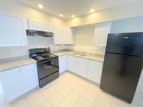A black refrigerator stands in a kitchen with white cabinets and a marble countertop.