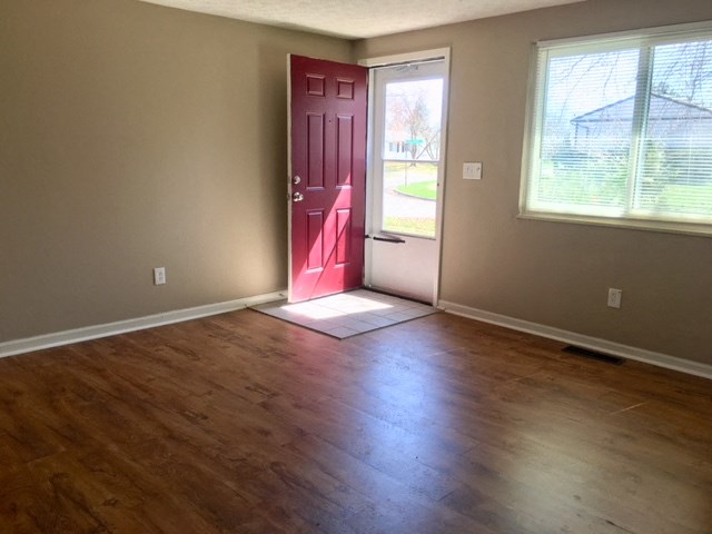 an empty living room with a red door and wood floors