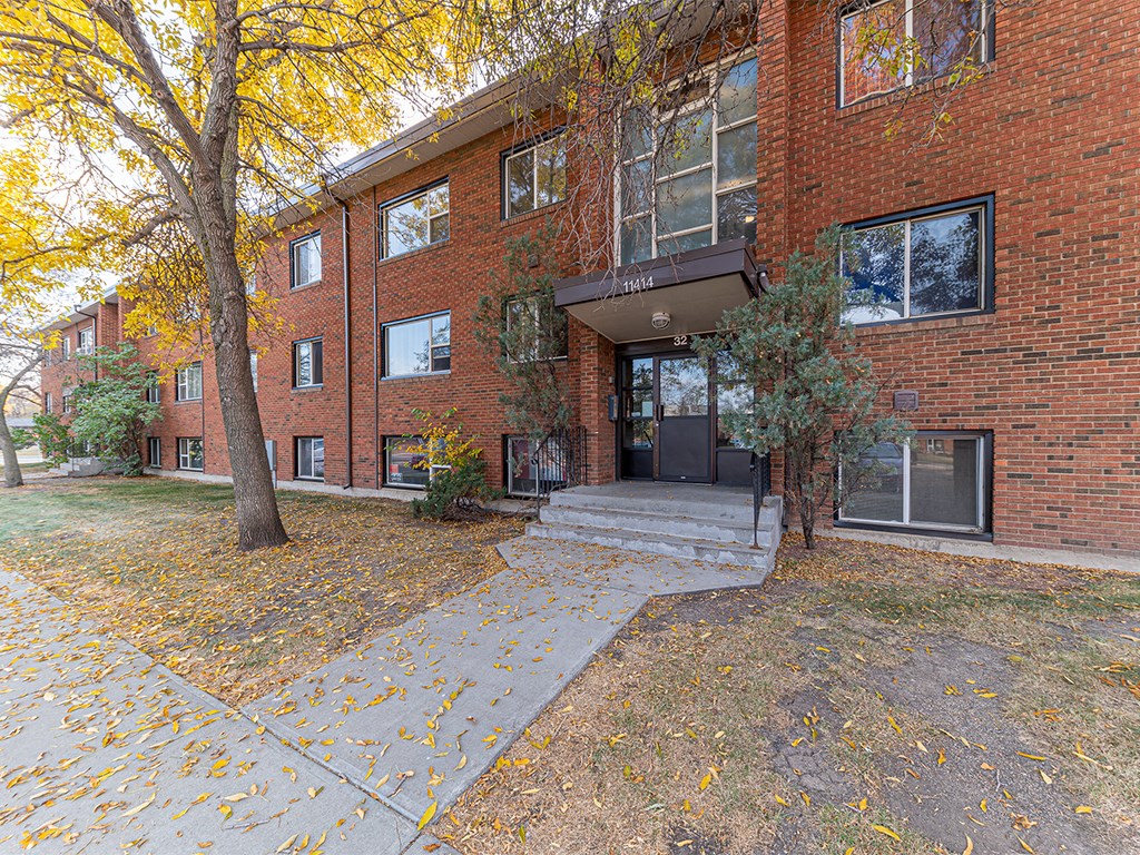 the front entrance of a brick apartment building with a sidewalk and trees
