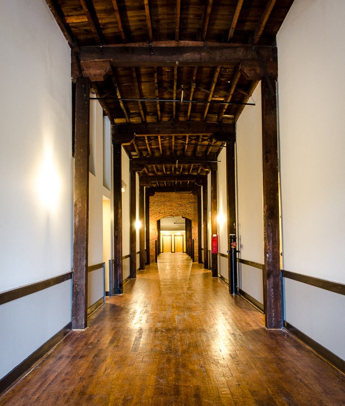 the long hallway of the building has a wood floor and pillars