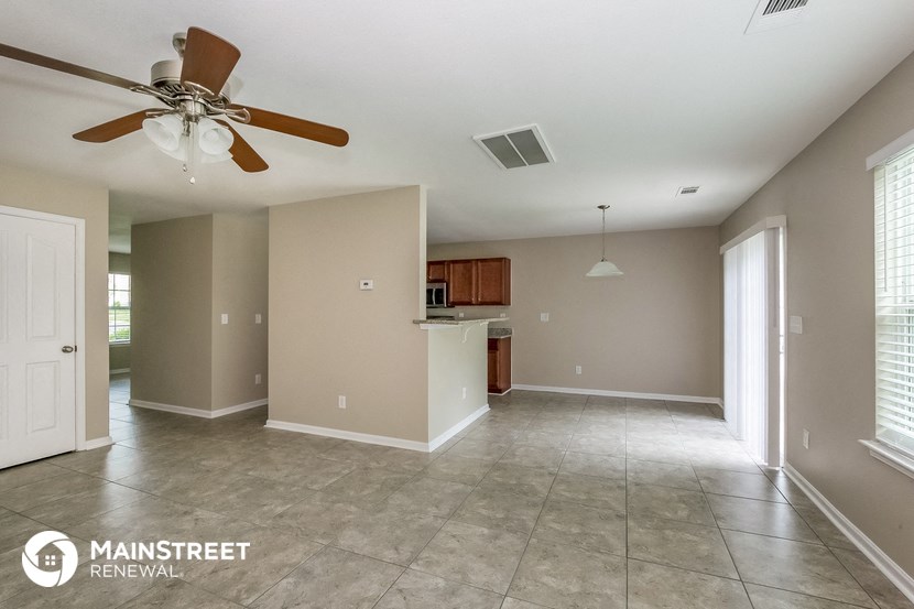 an empty living room with a ceiling fan and a kitchen