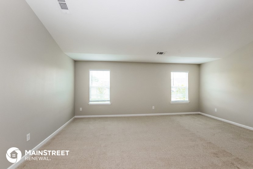 the bedroom of an apartment with carpet and two windows