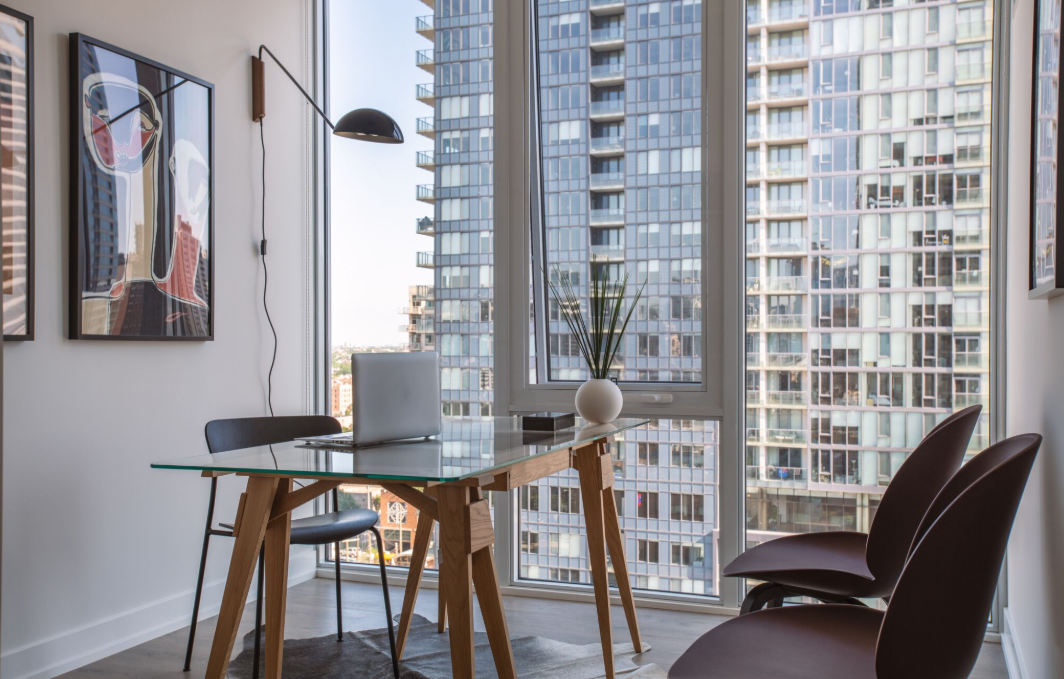 a desk with a laptop and chairs in a room with a window