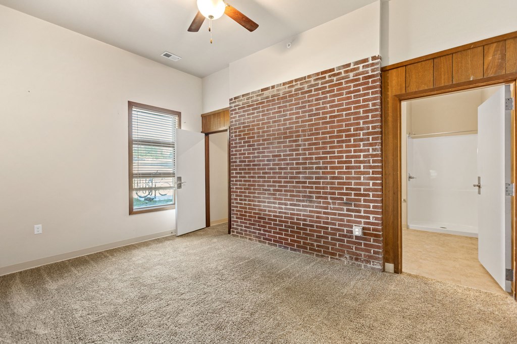 an empty living room with a brick wall and a door to a bathroom