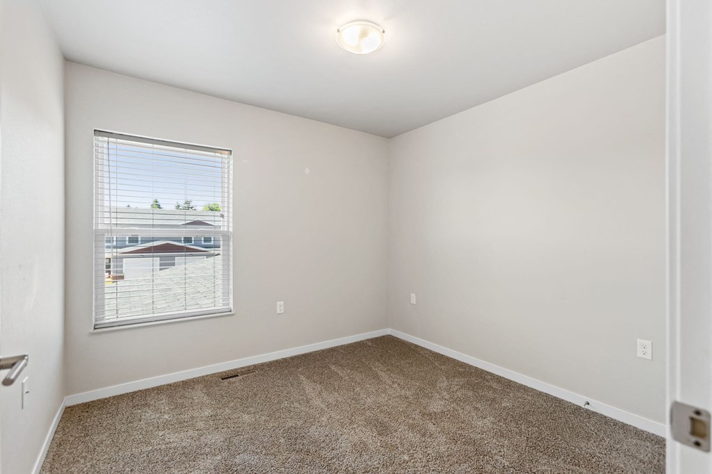 an empty bedroom with a window and carpeted floors