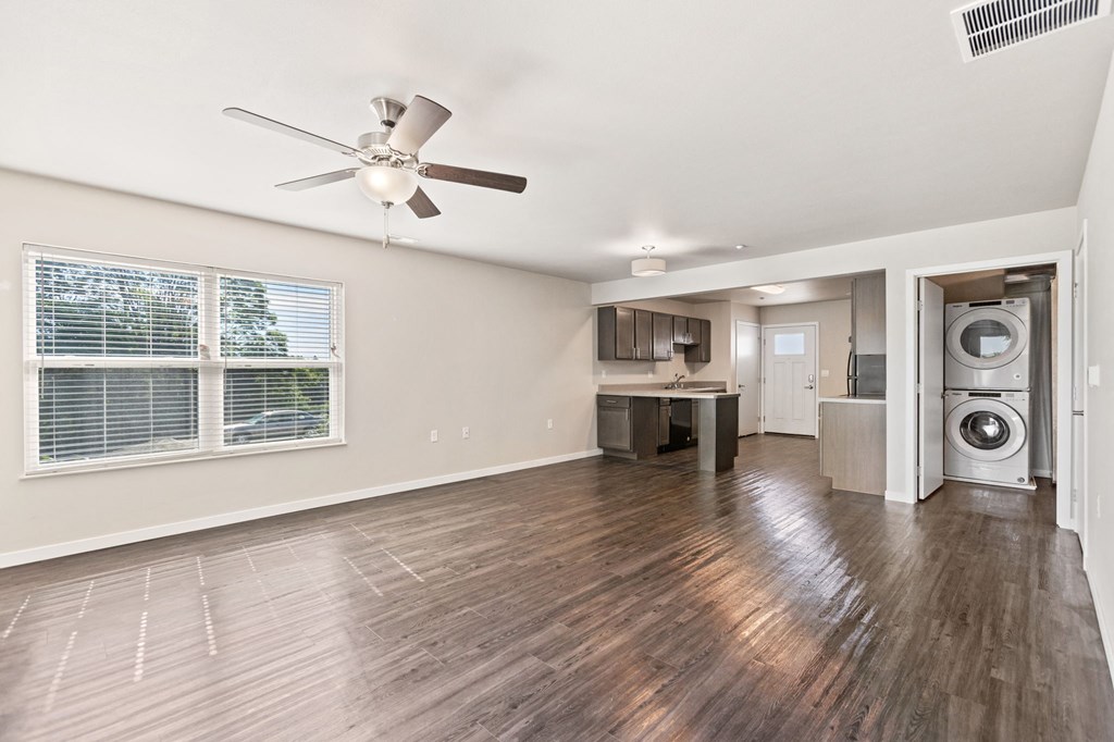an empty living room with a kitchen and a ceiling fan