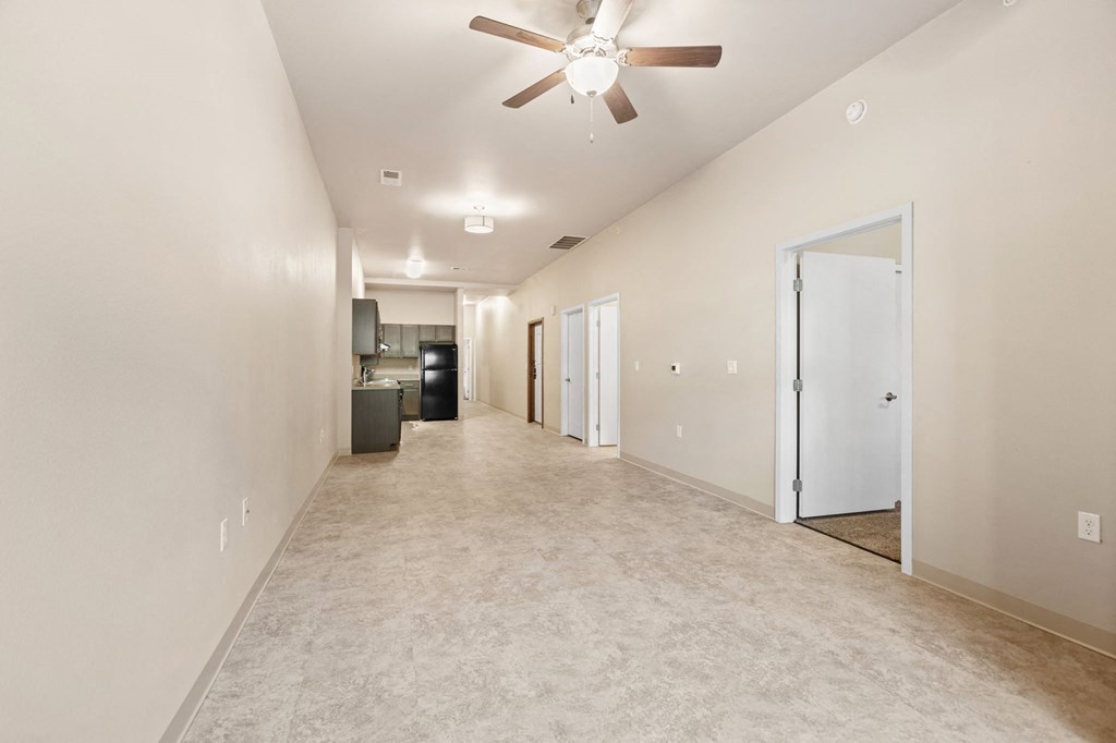 a long carpeted hallway with a ceiling fan and a door to a kitchen