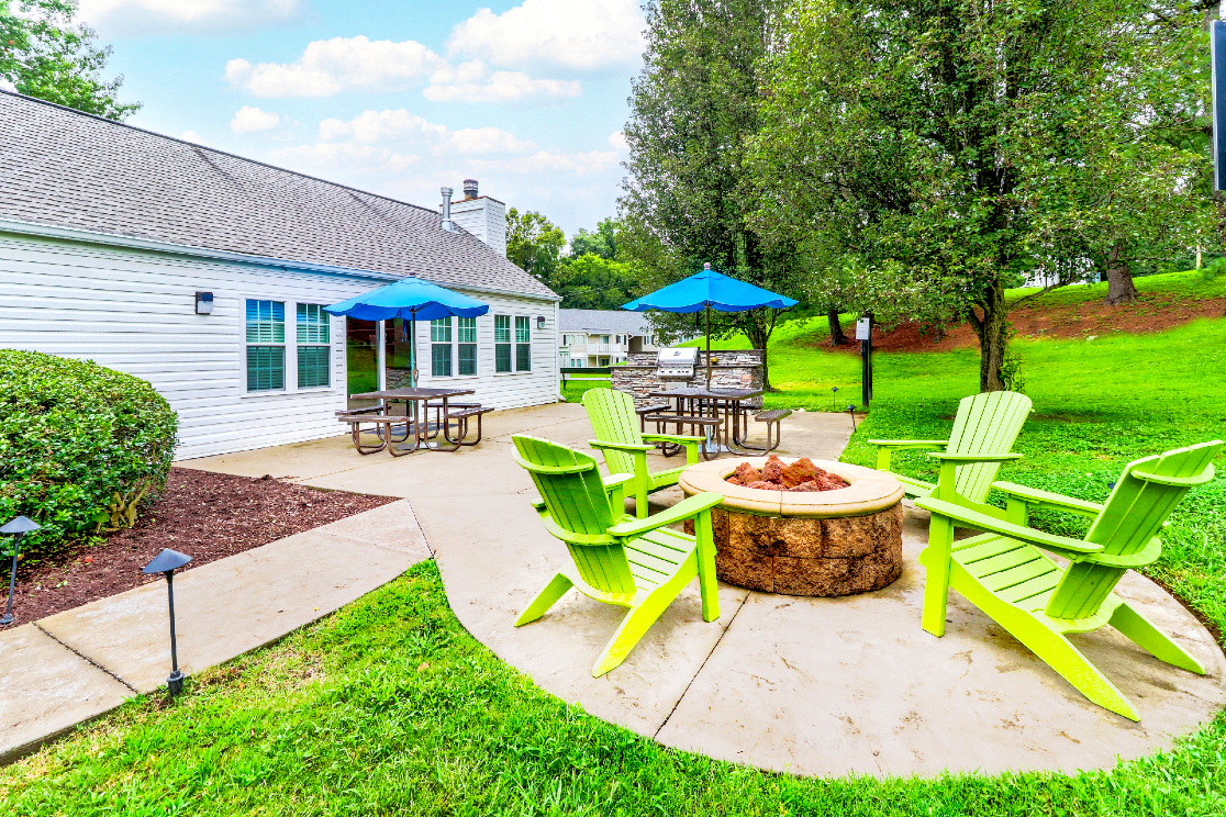 the backyard has a fire pit with green chairs and umbrellas