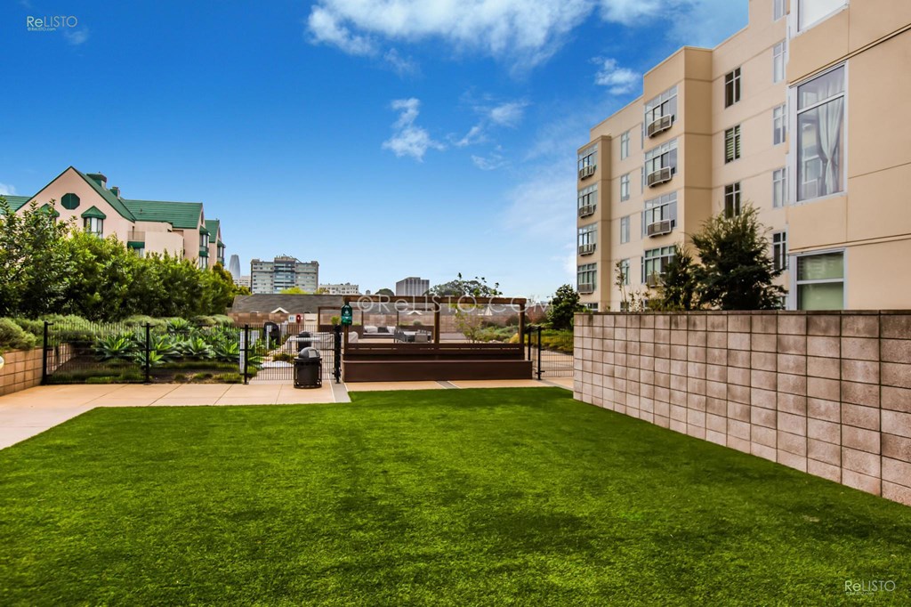 a backyard with a green lawn and a wall with apartments in the background