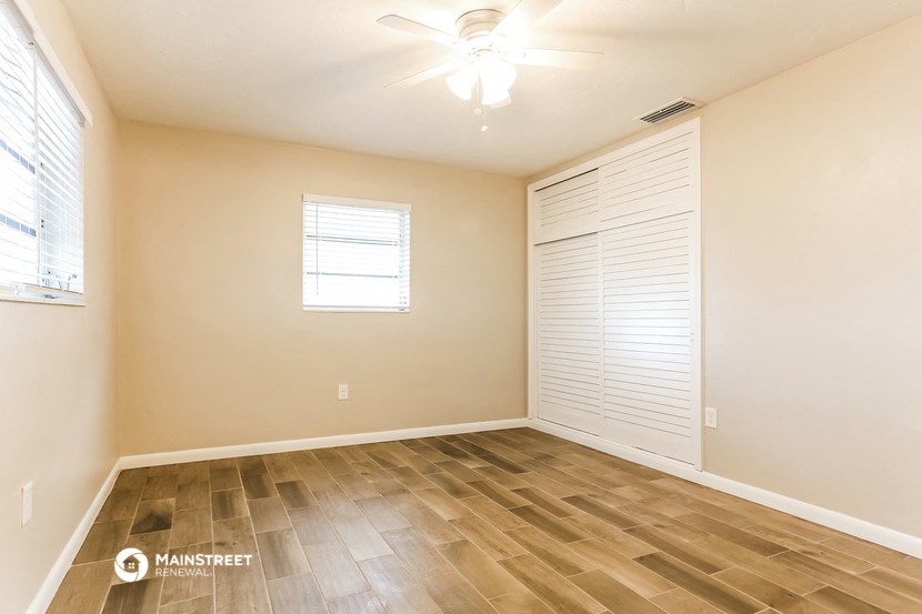 the spacious living room with wood flooring and a ceiling fan