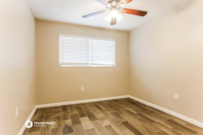 the spacious bedroom with hardwood flooring and a ceiling fan