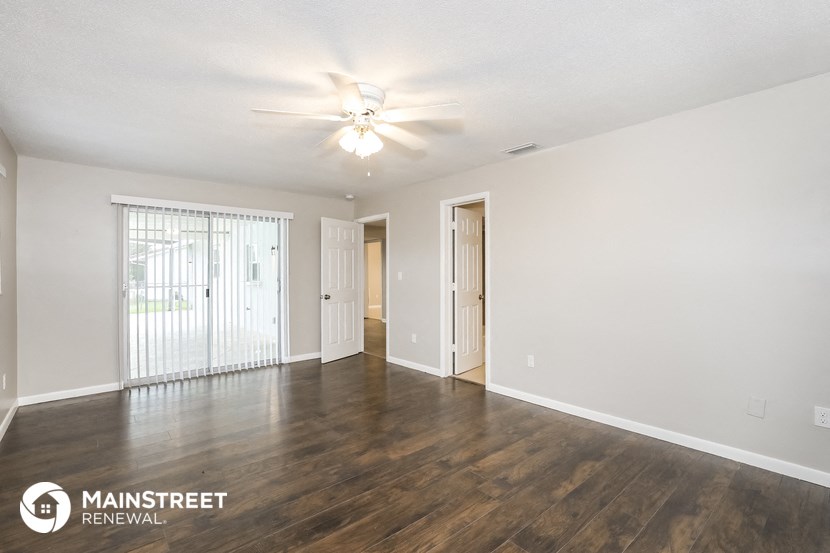 the spacious living room with wood flooring and a ceiling fan