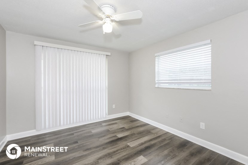 the spacious living room has a ceiling fan and wood flooring