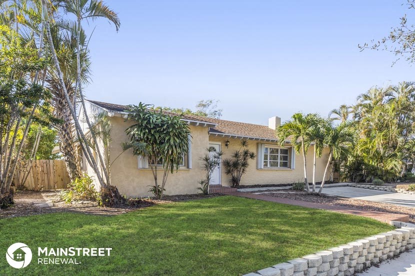 a yellow house with a lawn and palm trees