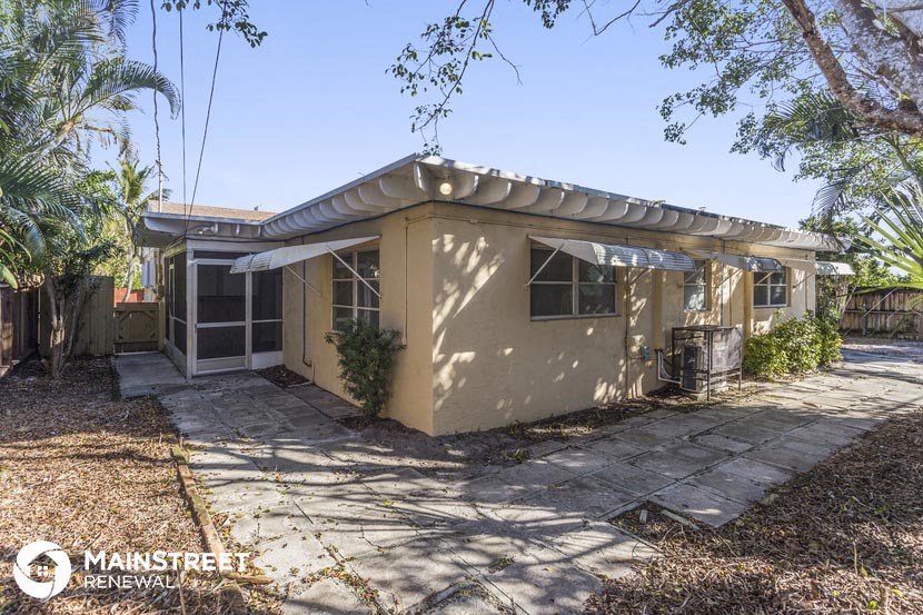 a small beige house with a patio and a driveway