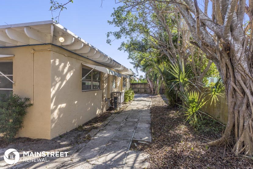 a small beige house with a sidewalk and trees