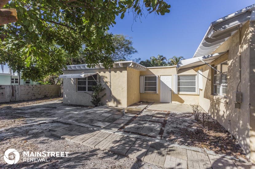 a small yellow house with a driveway and a tree