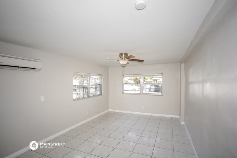 an empty living room with a ceiling fan and two windows