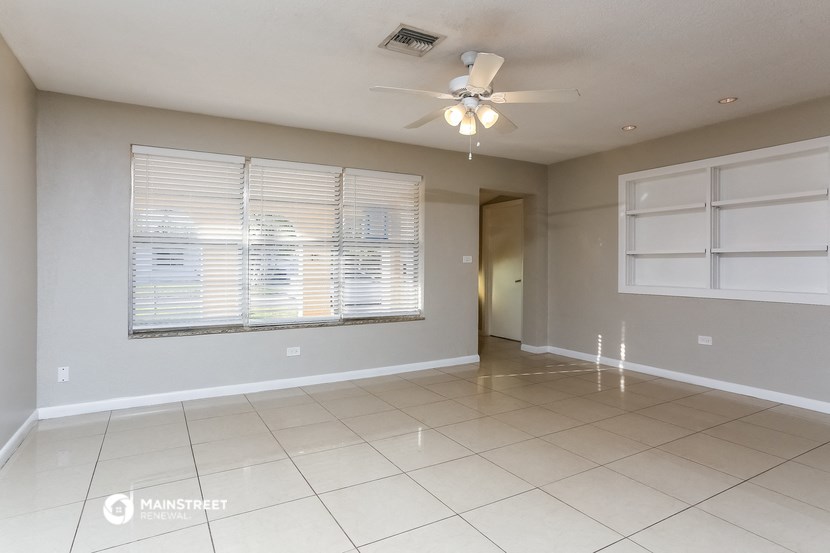 an empty living room with a large window and a ceiling fan