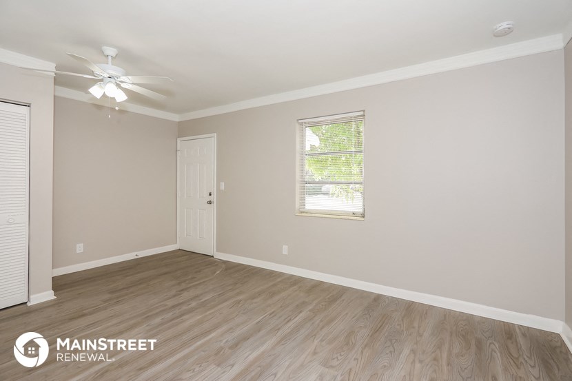 the spacious living room with wood flooring and a ceiling fan