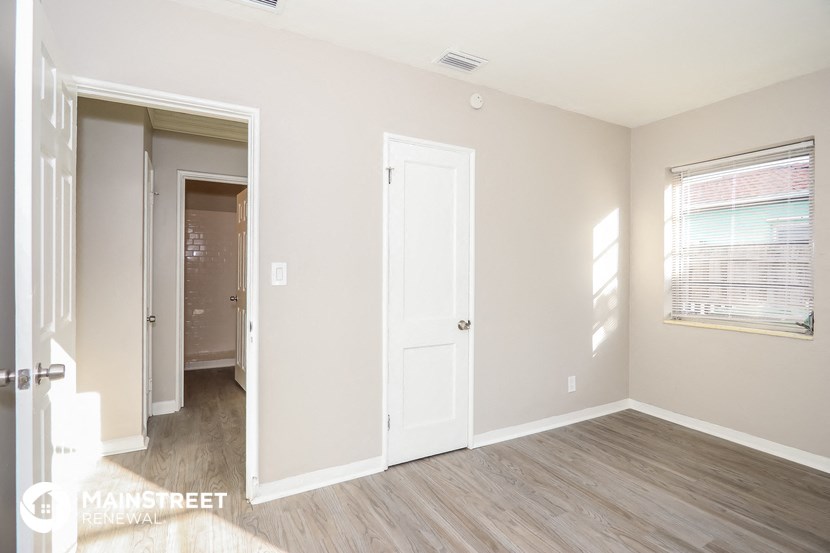 a bedroom with a white door and a hallway to a closet and a door to