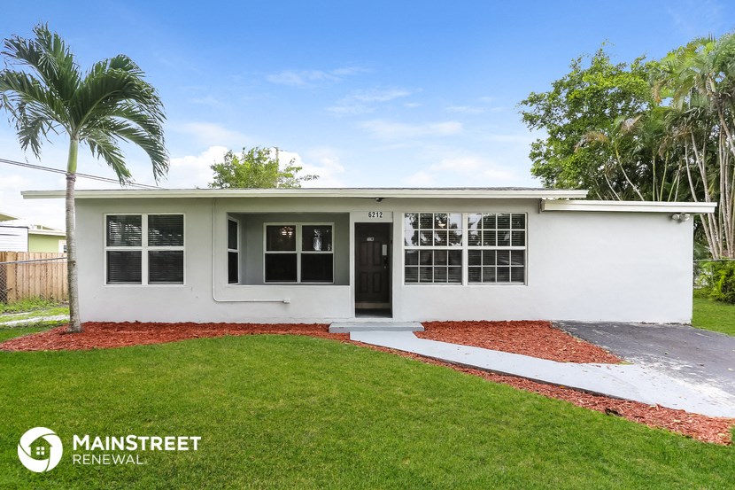 a small white house with a lawn and palm tree