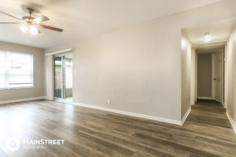 the spacious living room with wood flooring and a ceiling fan