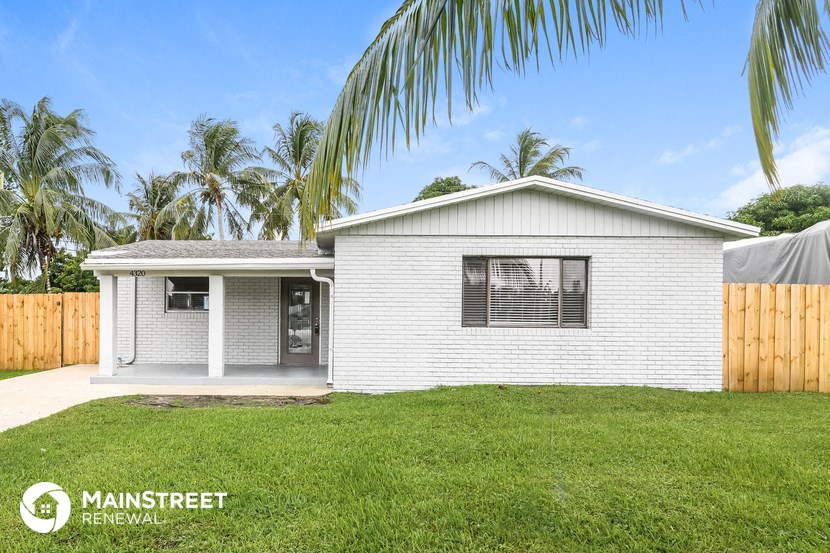 a small white house with a lawn and palm tree