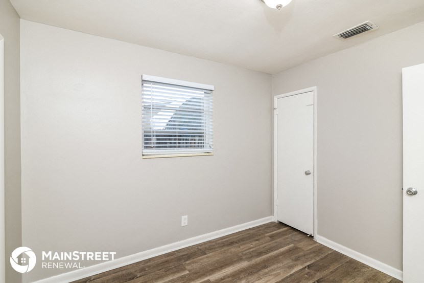 a bedroom with white walls and wood flooring and a window