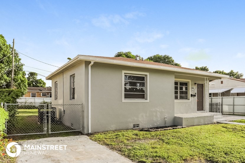 a small gray house with a yard and a chain link fence
