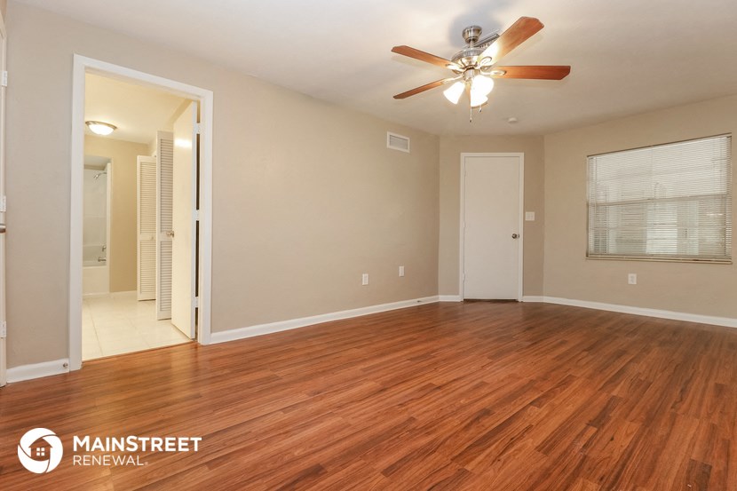 the spacious living room with hardwood flooring and a ceiling fan