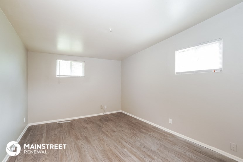the living room with wood flooring and white walls and two windows