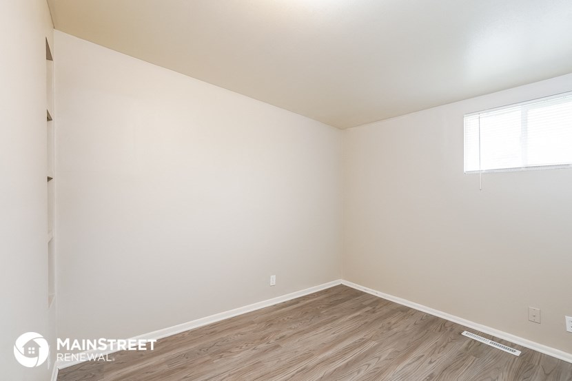a bedroom with white walls and wood flooring and a window