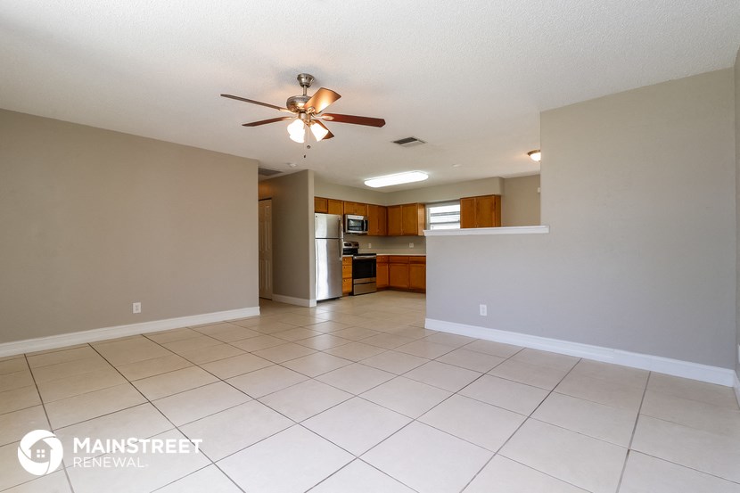 an empty living room with a ceiling fan and a kitchen
