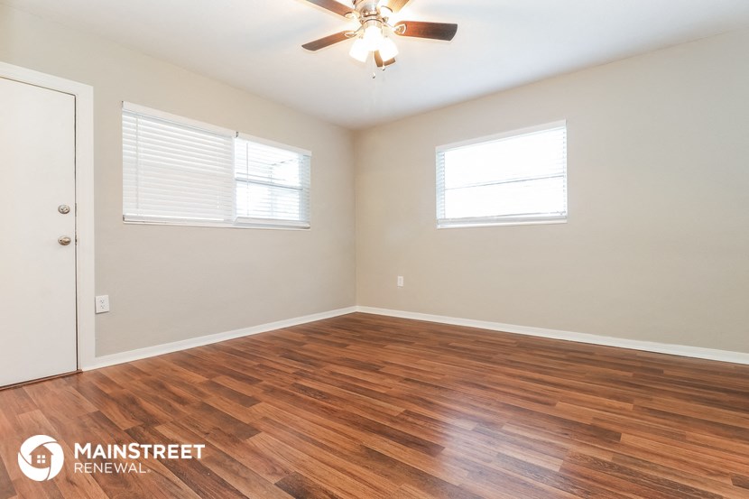 the spacious living room with hardwood flooring and a ceiling fan