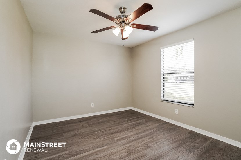 the spacious living room with wood flooring and a ceiling fan