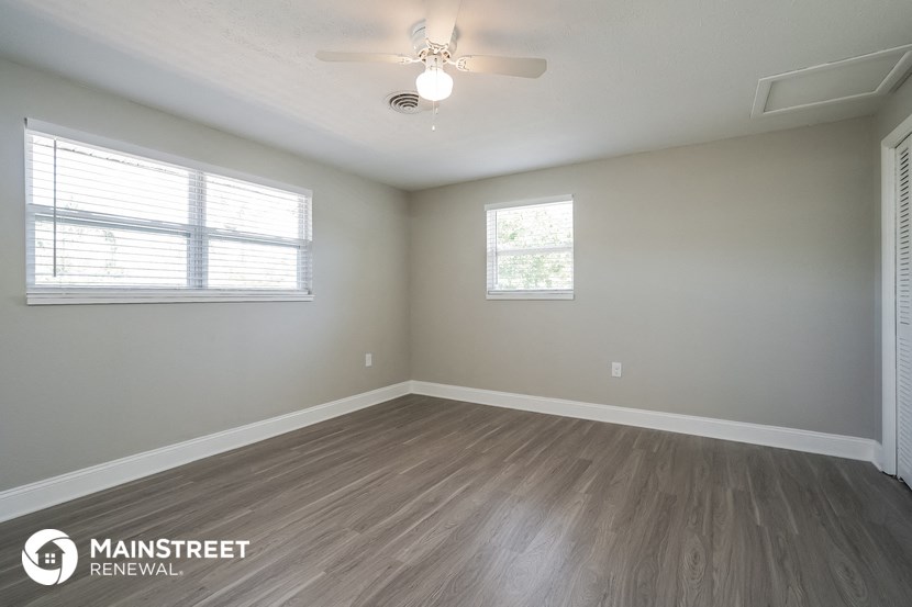 the spacious living room with wood flooring and a ceiling fan
