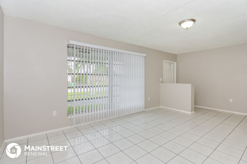 a spacious living room with a large window and a white tile floor