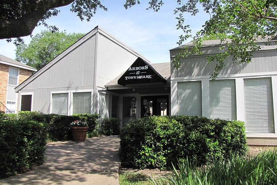 a white building with a sidewalk and bushes in front of it
