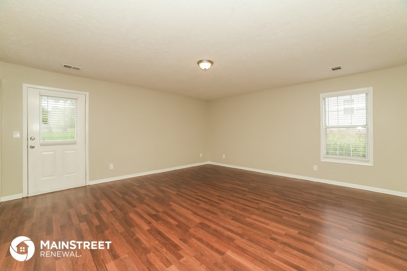 the spacious living room with wood flooring and a white door