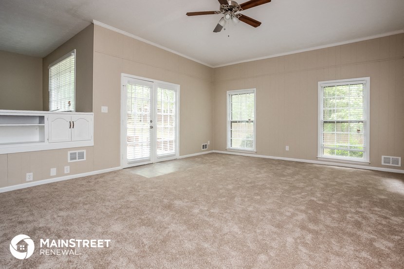 an empty living room with a ceiling fan and windows