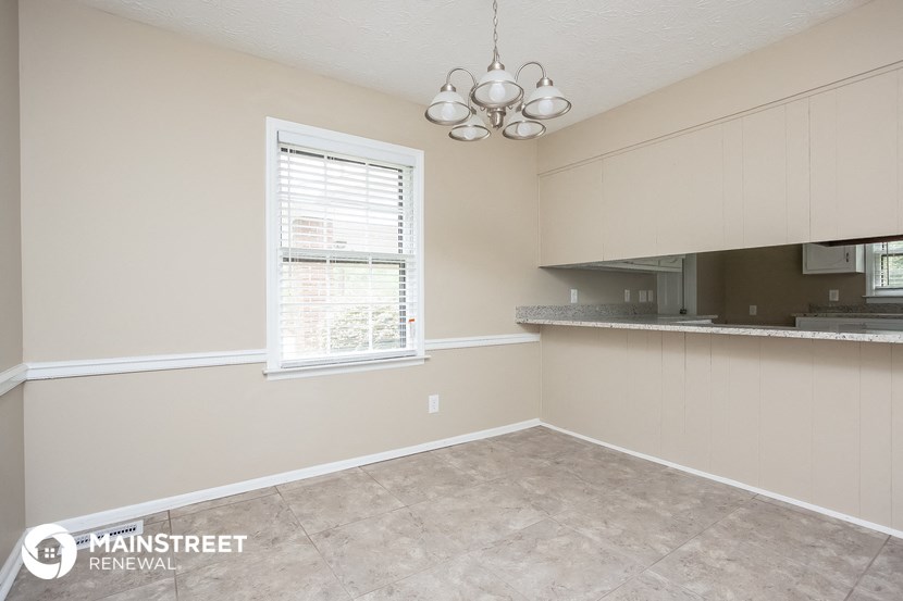 an empty living room with a kitchen and a window