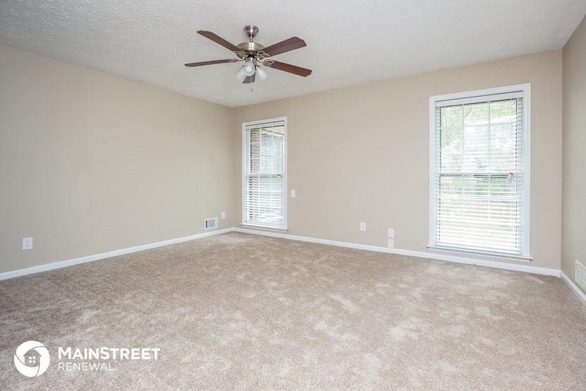 an empty living room with a ceiling fan and two windows
