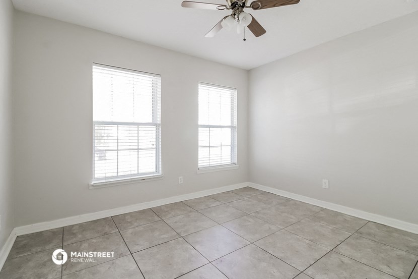 the spacious living room with two windows and a ceiling fan