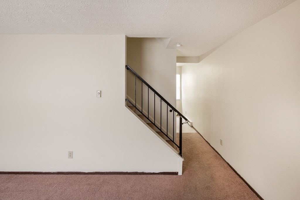 the upstairs of a home with a staircase and white walls and carpet