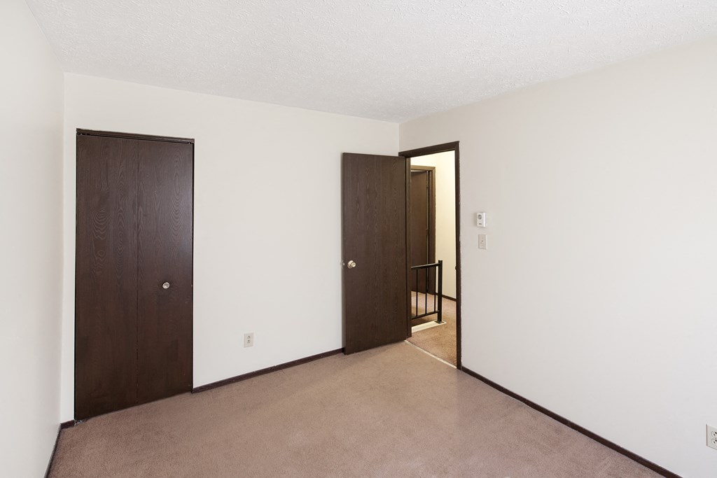 an empty living room with a door to a hallway and a doorway into a bedroom