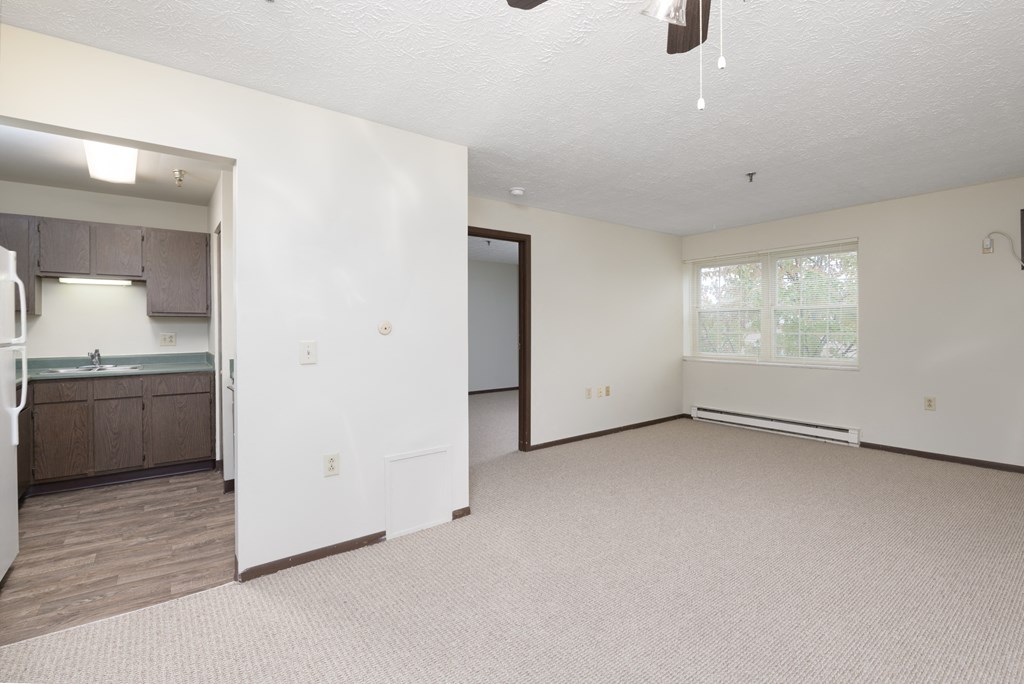 an empty living room with a kitchen in the background