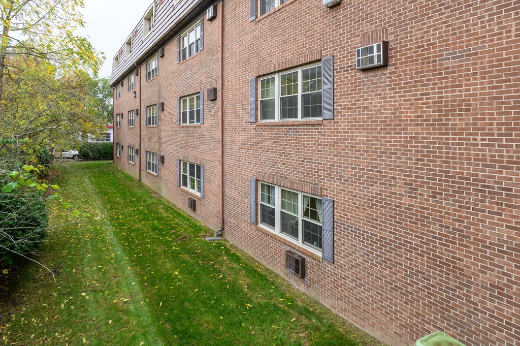 the side of a brick building with green grass and trees