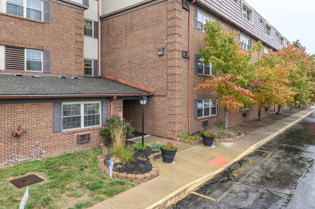 the front of a brick apartment building with a rain soaked sidewalk