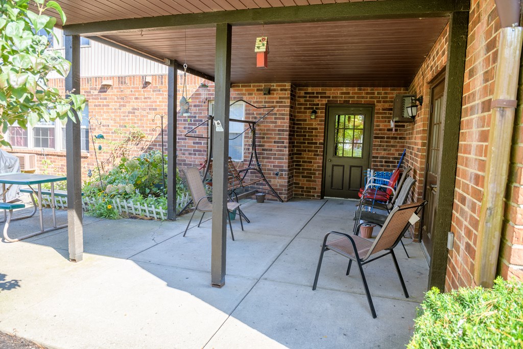 a covered patio with chairs and a door to a brick building